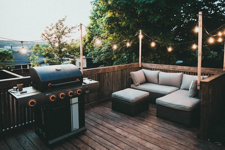 Terrassenbau Gemütlicher Außenbereich mit Grill und Sitzgelegenheit, umgeben von Lichtern und Bäumen.